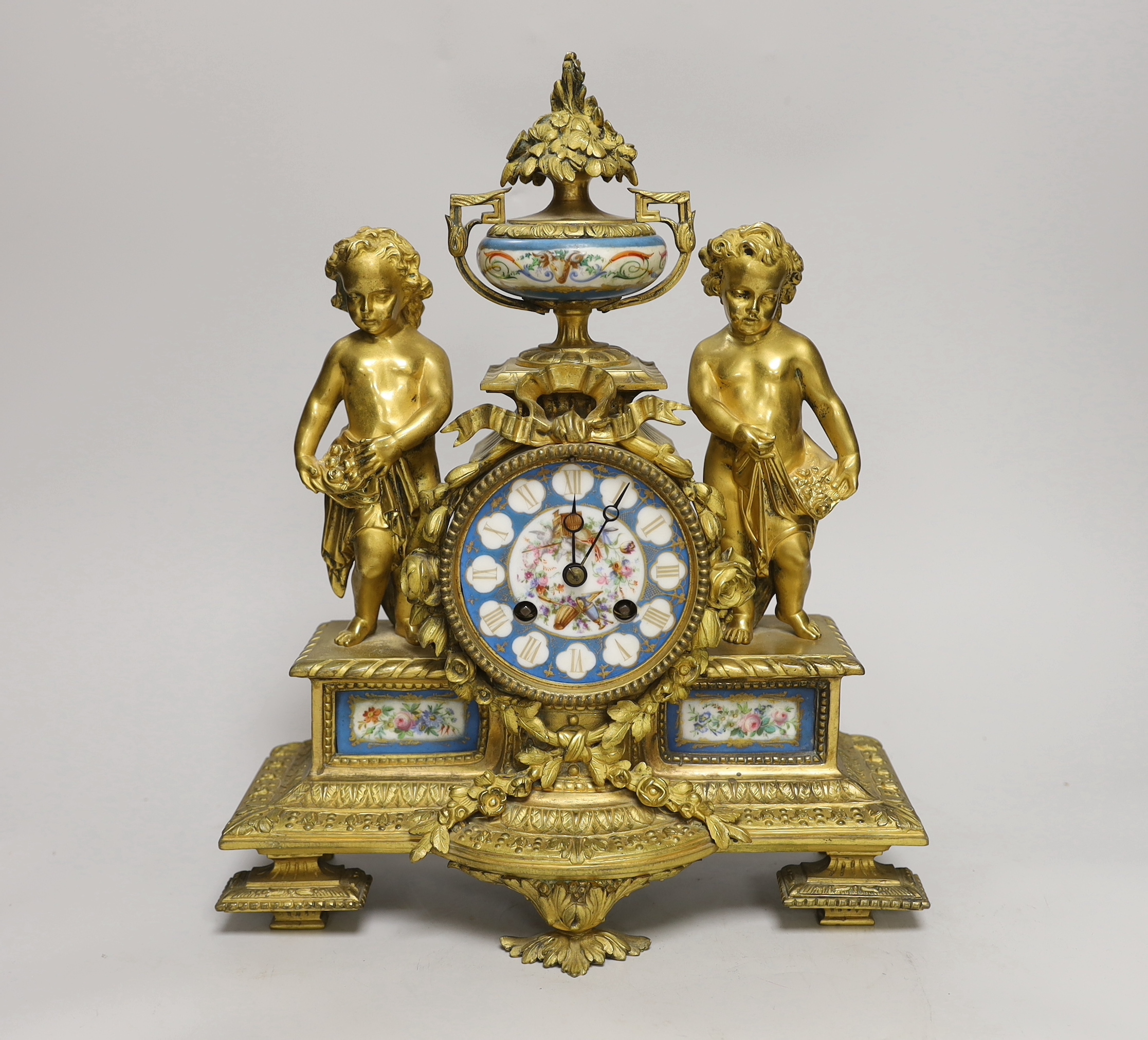 A French decorative ormolu putti mantel clock with porcelain clock face, side panels and urn